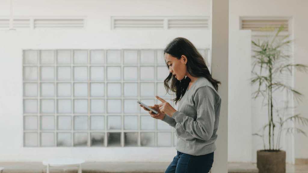 A person standing in front of a white wall and looking at their phone