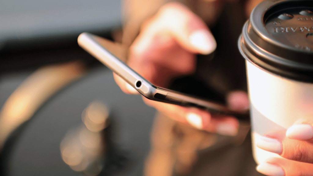 A person using a smartphone while sitting at a table with a cup of coffee 