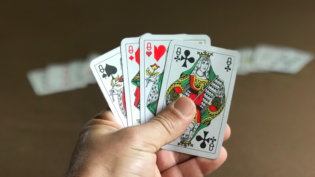 a hand holding four playing cards on a table