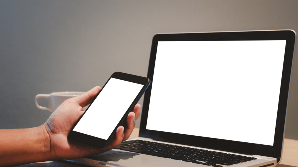 a person using a mobile phone on a desk next to a laptop and a mouse