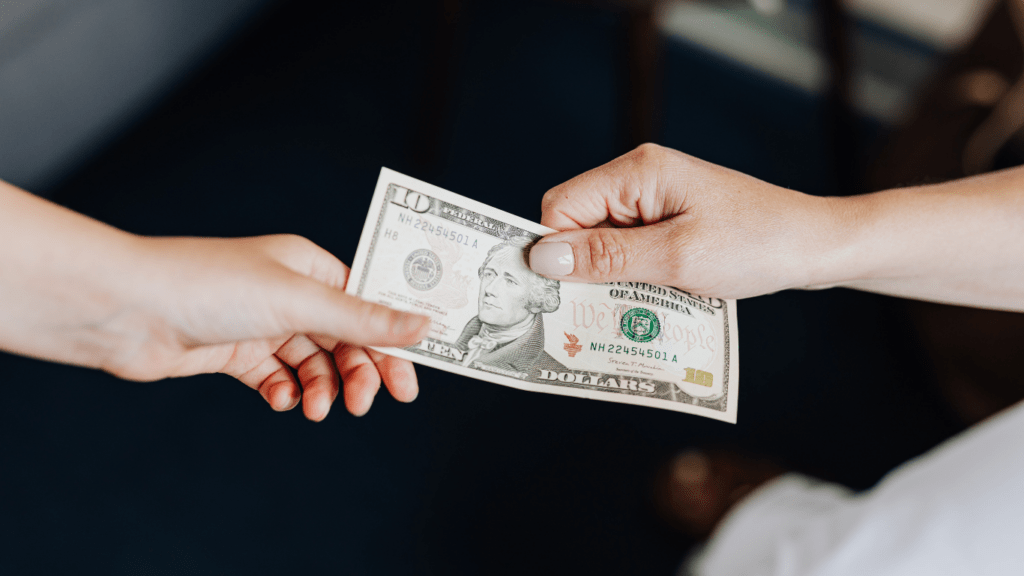 two people handing money to each other while sitting on a couch